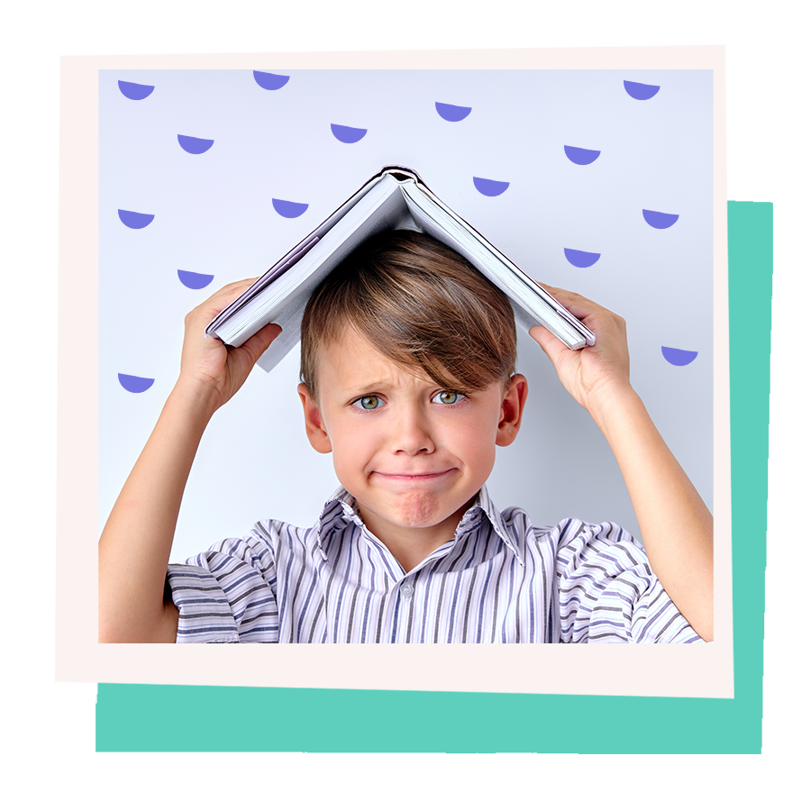 A boy holding a book over his head with a playful worried expression.