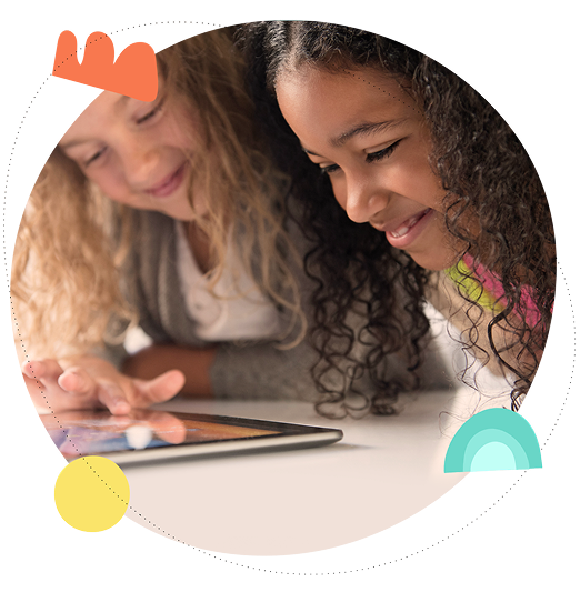 Two young girls smiling and using a tablet together in a playful learning environment.